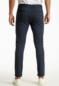 Marineblauwe slim-fit broek van gestructureerde stof, met achterzakken, opgerolde manchetten, en gecombineerd met witte sneakers.