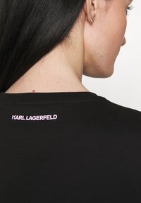 Camiseta de algodón negra con un logo en rosa "KARL LAGERFELD" en el cuello de la espalda, con cuello redondo y mangas cortas.
