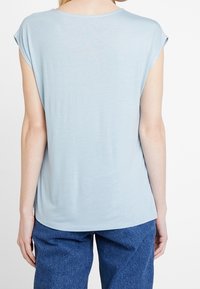 Top de manga corta azul claro, hecho de una tela suave, con un corte holgado y un escote redondeado. El dobladillo es ligeramente curvado en la parte de atrás.