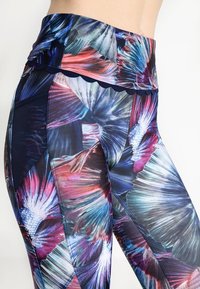 Tætsiddende leggings lavet af strækbart stof, med et farverigt blomstermønster primært i blå, pink og hvid, og en scalloped talje.