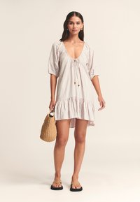 Lichtgewicht, gestreepte jurk met een diepe halslijn, korte pofmouwen en een gerimpelde zoom. Gecombineerd met een gehaakte tas en platte sandalen.