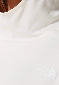 Camicia color crema a maniche corte con scollo tondo, caratterizzata da una finitura testurizzata e un logo bianco sul lato sinistro.