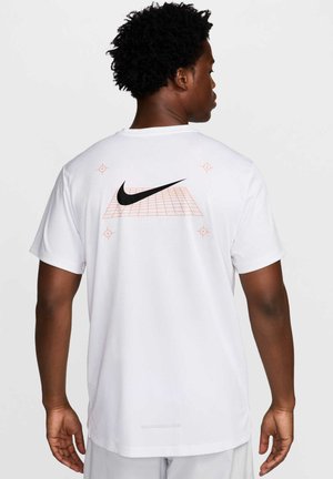 Mand set bagfra iført hvid Nike t-shirt med sort swoosh og orange gittergrafik på ryggen mod ensartet baggrund.
