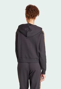 Černá mikina s kapucí a žebrovaným lemem a manžetami. Má kontrastní vzorované akcenty podél rukávů. Měkká, lehká textura látky.