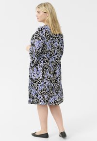 Vestido negro con un patrón de flores y estampado de leopardo en púrpura y blanco. Manga larga, corte relajado, a la altura de la rodilla, detalle plisado en el dobladillo.
