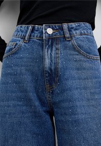 Jeans in denim blu con vita a metà, caratterizzati da cuciture a contrasto, cinque tasche e un motivo testurizzato sottile sul tessuto.