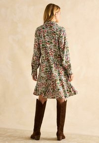 Blumengemustertes Kleid mit langen Ärmeln, Rüschensaum und Knopfverschluss. Getragen mit braunen Wildleder-Stiefeln bis zum Knie.