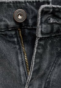 Jeans in denim nero con una zip in ottone visibile e un bottone metallico con branding inciso. Tessuto testurizzato con dettagli di cucitura classici.