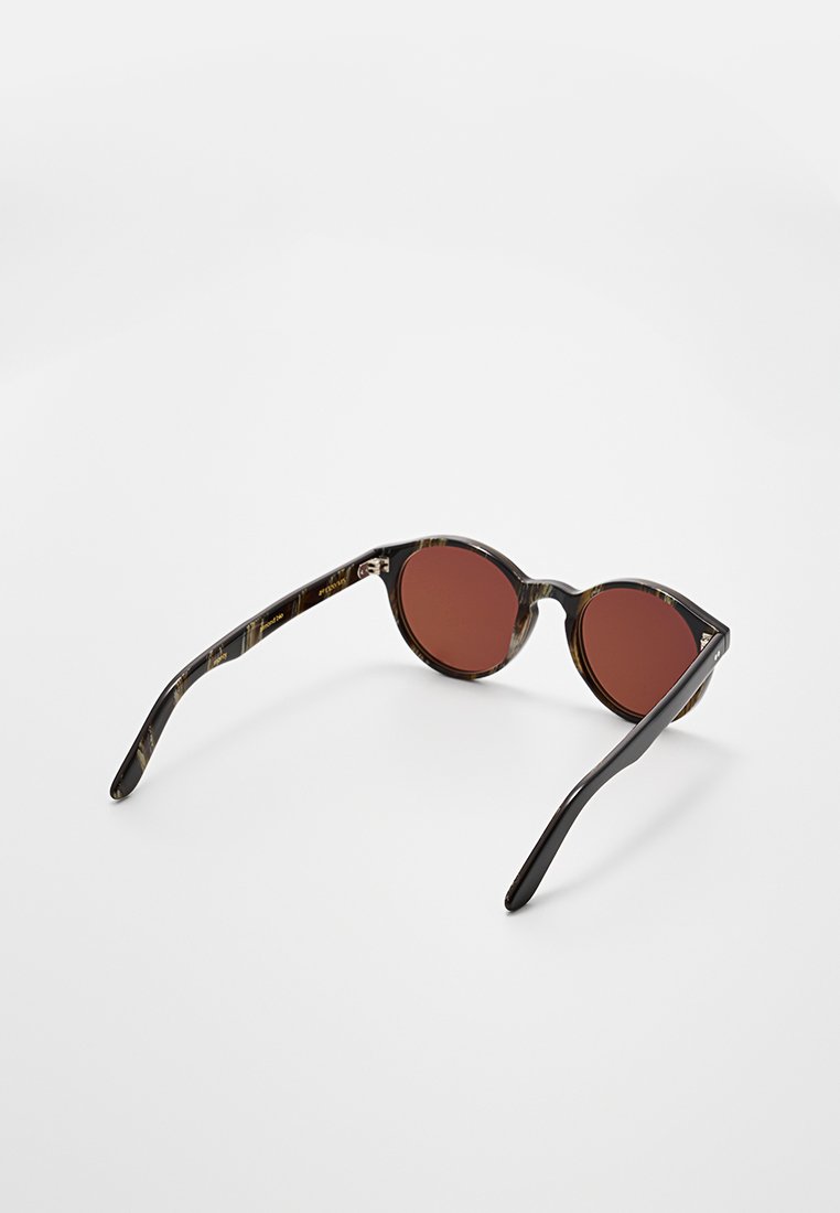 Runde Sonnenbrille mit einem Schildpattrahmen und dunkelroten Gläsern. Die Bügel weisen ein elegantes schwarzes Finish mit dezenten Mustern auf.