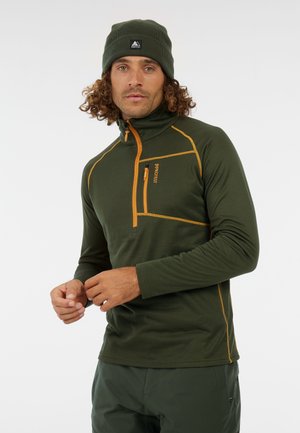 Groene longsleeve top met halve rits van textuurstof, oranje stiksel en een borstzak. Gecombineerd met een bijpassende donkergroene beanie.
