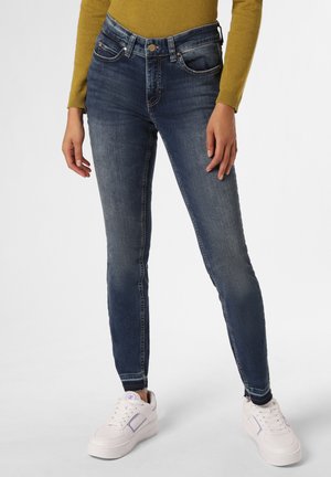 Dunkelblaue Skinny Jeans aus Denim, mit einem Fünf-Taschen-Design, vorderen Knöpfen und kontrastierendem stitching. Getragen mit weißen Sneakers.