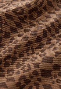 Brown fabric featuring a checkered leopard print pattern with varying shades of dark brown. The texture appears ribbed and woven.