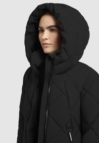 Must mustrakk lihtpuhutud jakk suure kapuutsiga, millel on ees lukku ja ribide detailid. Kangas näeb välja siledana ja mattlõikega.