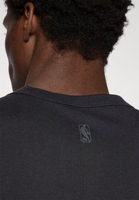 Ciemno-szary sportowy t-shirt z żeberkowym dekoltem i małym logo NBA nadrukowanym z tyłu, z gładkiego, teksturowanego materiału.