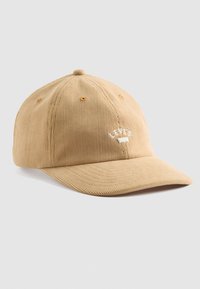Beige corduroy baseball cap with a rounded crown, curved visor, and white embroidered logo on the front. Six ventilation eyelets included.