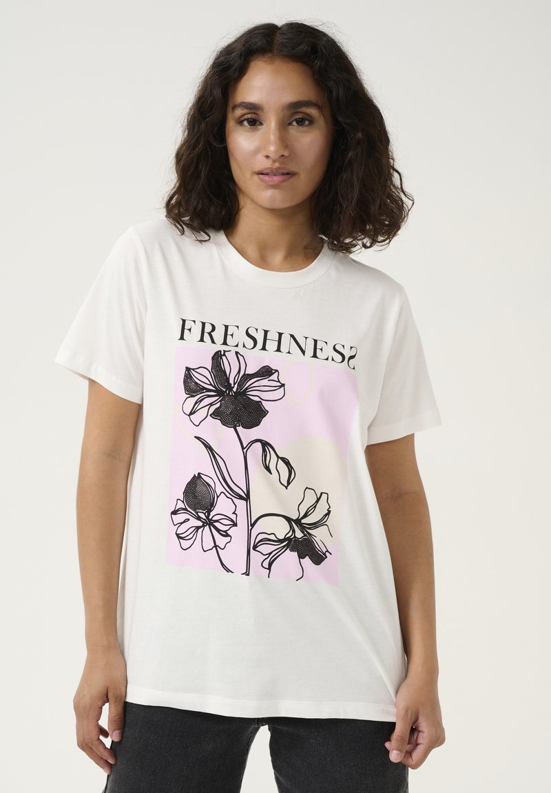 T-shirt en coton blanc avec un imprimé graphique de fleurs noires sur un fond rose, avec le texte "FRESHNESS?" en gras.