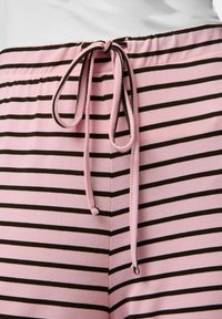Lichtroze gestreepte pyjamabroek met donkerbruine horizontale strepen. Bevat een taille met koord in bijpassende stof en is gemaakt van zacht, lichtgewicht materiaal.