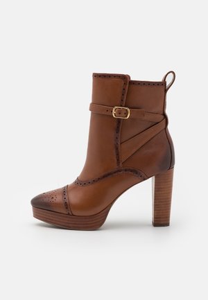 Bottine en cuir marron avec talon bloc en bois haut, perforations décoratives, une bride à boucle latérale et une languette à l'arrière.