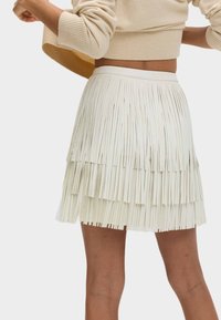 Jupe à franges en blanc cassé, comprenant des bandes de matière superposées, une taille lisse et une surface texturée pour plus de détails.