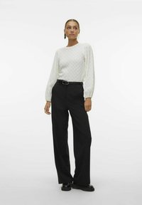Top bianco testurizzato a maniche lunghe con scollatura tonda, abbinato a pantaloni neri a vita alta e a gamba larga e scarpe platform nere.