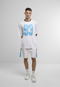 Fehér sportmez kék "93"-as számmal, fehér nadrággal, kék díszítéssel. Simább anyag, laza illeszkedés, kerek nyakkivágás.