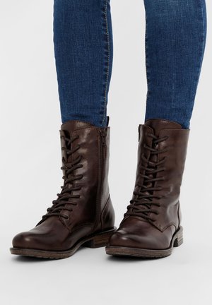 Bottes chelsea en cuir marron avec un laçage et une fermeture éclair latérale, dotées d'un bout rond et d'une semelle robuste pour la durabilité.