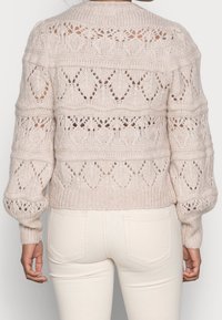 Jersey de punto beige claro con un patrón texturizado, que presenta un dobladillo acanalado y mangas abullonadas. Diseño calado con formas de diamante.