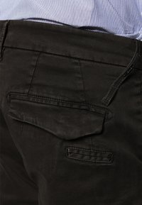 Schwarze Baumwollhosen mit Gesäßtaschen. Sie verfügen über einen strukturierten Stoff, kontrastierende Nähte und einen Bund mit einem kleinen Schlaufen-Detail.