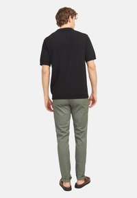 Polo shirt en tricot noir à manches courtes, pantalons vert olive, chaussures décontractées, avec des coutures visibles et des ourlets de pantalon retroussés. Design et texture simples.