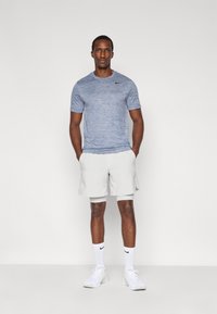 Αθλητική εμφάνιση Nike με μπλε κοντομάνικο πουκάμισο με μάλλινο σχέδιο και λευκά σορτς, συμπληρωμένη με λευκά αθλητικά παπούτσια και κάλτσες.