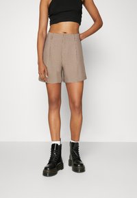 Shorts à carreaux marron et blanc avec une coupe ajustée, dotés de plis sur le devant et de poches latérales, associés à des bottes à lacets noires.