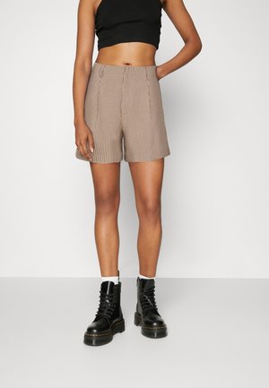 Shorts à carreaux marron et blanc avec une coupe ajustée, dotés de plis sur le devant et de poches latérales, associés à des bottes à lacets noires.