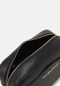Bolso de cuero negro con superficie texturizada, cremallera dorada y detalle de logo. Presenta un compartimento con cremallera para un almacenamiento seguro.