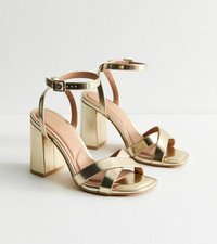 Gold metallic sandals with a block heel and ankle strap. Features crossed front straps and a smooth, shiny texture.