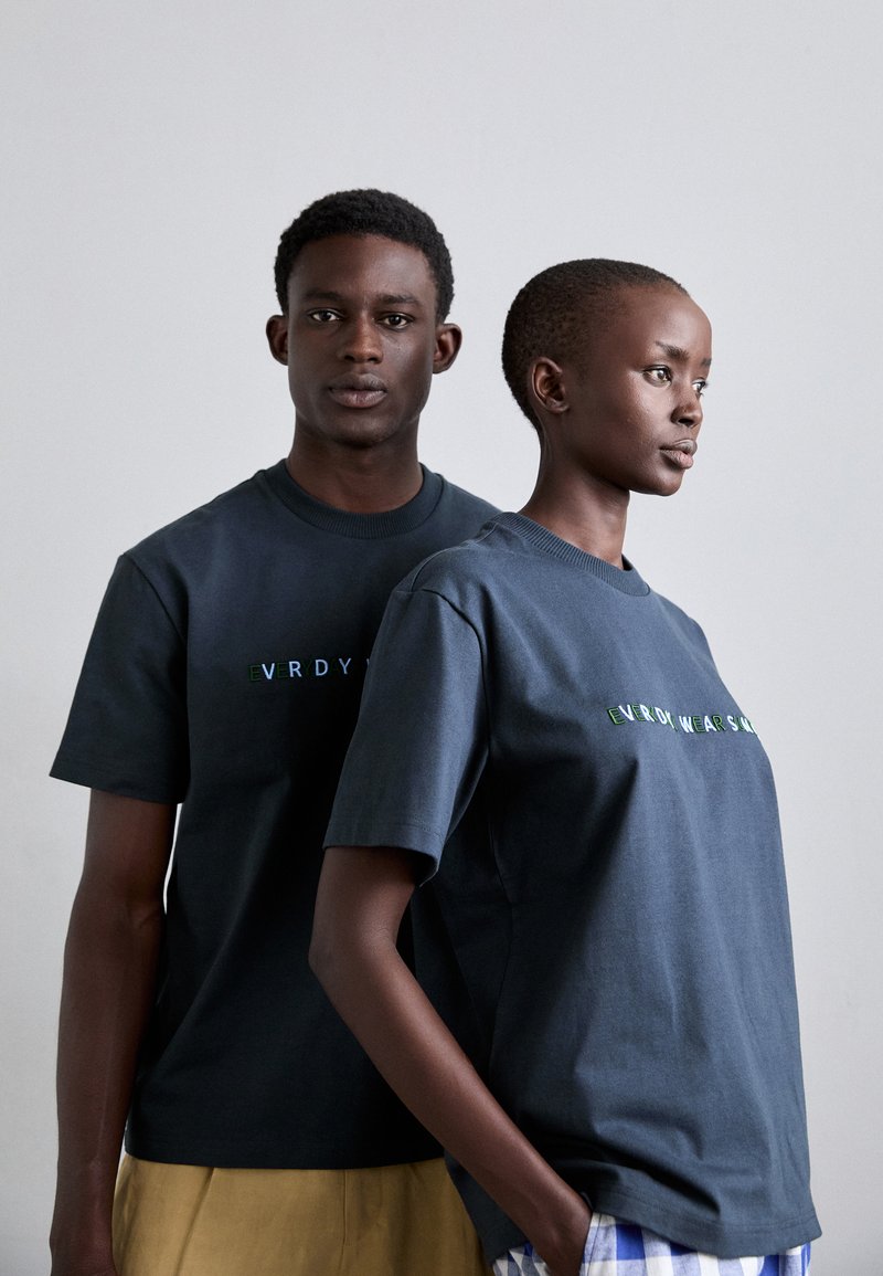 Dark blue cotton t-shirts with short sleeves, featuring a graphic text in multicolored lettering across the chest, worn by two models.