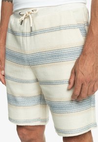 Pánské kraťasy v krémové barvě s vodorovnými světle modrými a béžovými pruhy. Materiál vypadá jako tkaný, s páskem na stažení a bočními kapsami.