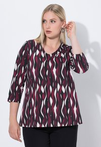 Tryckt topp med en vågig mönster i mörkröd, svart och vit. Den har trekvartslånga ärmar och rund halsringning. Mjuk textur.