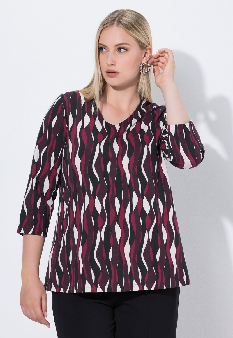 Tryckt topp med en vågig mönster i mörkröd, svart och vit. Den har trekvartslånga ärmar och rund halsringning. Mjuk textur.