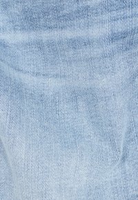 Zblízka na světlemodrou denimu, která vykazuje tkanou strukturu a diagonální vzor tkaní.