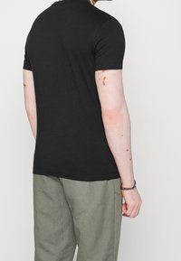 T-shirt noir à manches courtes en coton doux, avec un col rond et une coupe ajustée, présenté de dos sur un fond neutre.