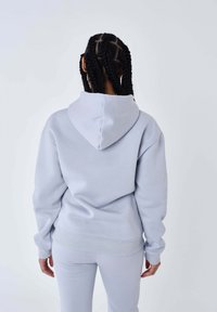 Lichtgrijze hoodie met een grote capuchon, geribbelde manchetten en zoom. De stof lijkt zacht en heeft een relaxte pasvorm, gedragen met bijpassende onderkleding.