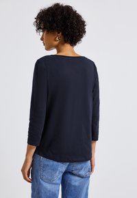 Haut à manches longues bleu marine en tissu doux et lisse avec un décolleté large et un ourlet arrondi, associé à un jeans bleu clair.