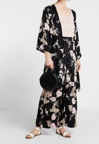 Sort kimono med blomsterprint i pink og beige mønstre, kombineret med en lyserød top og blomstrede bukser. Tilbehør inkluderer en rund sort taske og hvide sandaler.