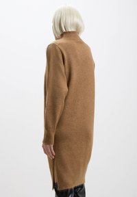 Abito in maglia marrone con colletto alto, maniche lunghe, spacco laterale e una texture morbida. Design semplice e morbido.