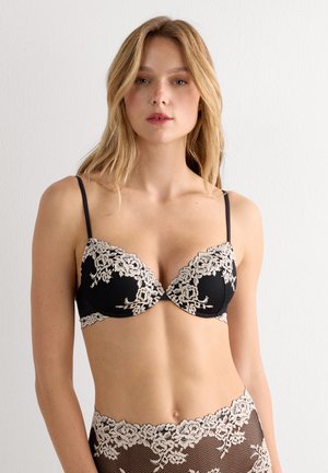 Schwarzer Spitzen-BH mit beiger Blumenstickerei, ausgestattet mit vorgeformten Körbchen, verstellbaren Trägern und einer glatten Textur. Für eine zeitgemäße Passform entworfen.