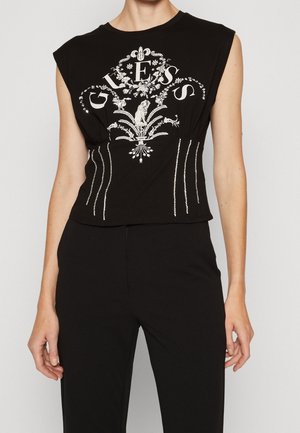 Top noir court sans manches avec un design graphique argenté comportant des détails ornés et des lettres. Fabriqué en coton doux avec un léger stretch.