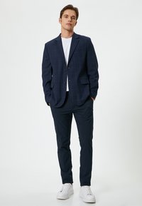 Mörkblå rutig blazer med två knappar, matchad med mörkblå byxor och vita sneakers. Slätt tyg, strukturerad design och smal passform.