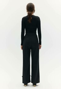 Czarna bluzka z długim rękawem w połączeniu z czarnymi spodniami typu wide-leg o wysokim stanie. Gładka faktura tkaniny z subtelnymi detalami przy brzegach i akcentami na obuwiu.