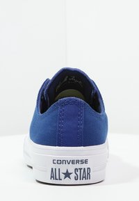 Niebieskie trampki na płaskiej, białej gumowej podeszwie. Posiadają wyściełany kołnierz, kontrastowe szwy oraz logo "Converse All Star" na pięcie.