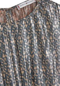 Faltendes Kleid in metallischem Blau und Roségold, mit einem abstrakten Muster. Der Ausschnitt hat eine subtile Öffnung auf der Rückseite, die die Stoffstruktur zur Geltung bringt.